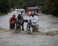 Personas cruzan con dificultad la carretera que se encuentra inundada producto de las intensas lluvias, ayer en San José de Ocoa (República Dominicana).