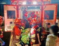 Imagen de bomberos subiendo a upersonas heridas al interior de una ambulancia.