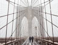 Fotografía de archivo en la que se registró a un par de transeúntes al cruzar el puente de Brooklyn, bajo una tormenta de viento y nieve, en Nueva York