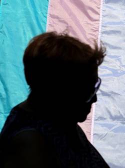 Una persona detrás de una bandera que promueve el orgullo trans.