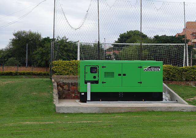 Imagen de un generador eléctrico al pie de una cancha de fútbol.
