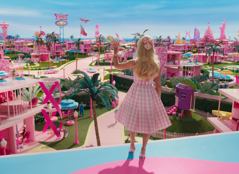 Margot Robbie caracterizada como la icónica muñeca de la empresa Mattel parada en la terraza de su casa de ensueños saludando a las Barbies de Barbieland.