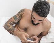 Hombre viendo el celular en una cama.