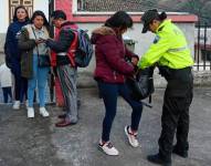 Una mujer policía revisa a una persona que porta una mochila.