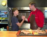 Un niño y su padre estrechando manos ante una parrilla.