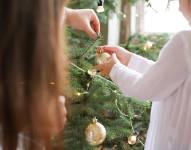 Foto referencial de una niña retirando la decoración navideña del árbol.