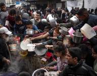 Niños y adultos con ollas pidiendo comida.