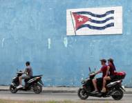 AME4388. LA HABANA (CUBA), 26/04/2023.- Motociclistas cruzan frente a un mural con la bandera cubana hoy en La Habana.