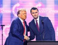 Esta foto, tomada el 22 de diciembre de 2024, muestra al activista de derecha Charlie Kirk (der.) estrechando la mano del presidente estadounidense Donald Trump mientras este habla en el escenario del America Fest 2024 en Phoenix, Arizona.
