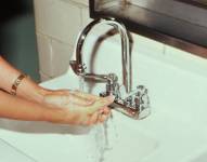 Imagen de una persona lavándose las manos con el agua de un grifo en un baño.