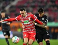 Mërgim Berisha (i), autor del único tanto que le dio la victoria al Augsbrugo, disputa el esférico ante el defensa ecuatoriano Piero Hincapié, del Bayer Leverkusen.