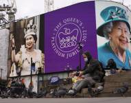 Un hombre alimenta a las palomas y a sus espaldas se ve una pantalla en Piccadilly Circus para celebrar el 70 aniversario del ascenso al trono de la reina Isabel de Gran Bretaña, en Londres, el domingo 6 de febrero de 2022.