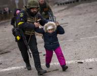 Un policía ucraniano ayuda a una niña que corre ante los estallidos de artillería cercana, mientras la población civil abandona Irpin, en las afueras de Kiev, Ucrania, el lunes 7 de marzo de 2022. (AP Foto/Emilio Morenatti) REFERENCIAL