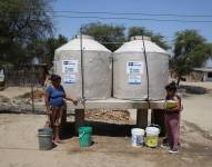 Mujeres llenan baldes con agua de los bidones instalados por Acción contra el Hambre, el 6 de septiembre de 2023 en el asentamiento humano de Mocará, departamento de Piura (Perú).