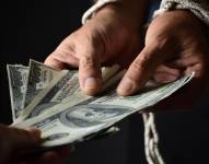 Imagen referencial. Foto de una persona entregando varios billetes de 100 dólares.