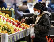 Una mujer con una mascarilla para el coronavirus selecciona frutas en el mercado de Reading Terminal en Filadelfia.
