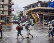Personas caminan por una calle encharcada debido a las fuertes lluvias en el balneario de Acapulco, estado de Guerrero.