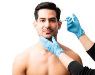 Closeup of doctor's hands injecting botox into the skin of male model on white background