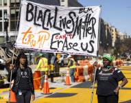 Un par de manifestantes afroestadounidenses fueron registradas este lunes, 10 de marzo, al sostener un cartel en protesta por la eliminación de la Plaza Black Lives Matter (Las vidas negras importan), mientras cuadrillas de obreros levantan los bolardos que hacían peatonal esta zona de Washington DC (EE.UU.).