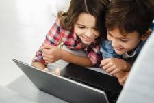 Imagen referencial de dos niños aprendiendo mientras sonríen frente al computador.