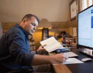 Imagen referencial de hombre estudiando desde casa con computadora y libros.