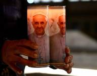 Un fiel de Bolivia sostiene velas del Papa Francisco cerca de una estatua del Papa Juan Pablo II fuera del hospital Gemelli donde el Papa Francisco está hospitalizado para pruebas y tratamiento para la bronquitis en Roma, el 18 de febrero de 2025.