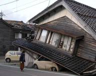 Una mujer observa una vivienda y vehículos dañados tras un fuerte terremoto en Tohi Town.
