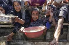 Palestinos desplazados internamente, incluidos niños, sostienen ollas para recibir alimentos de una cocina de caridad, en la ciudad de Gaza.