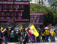 Personas caminan junto a varias pancartas que critican a jueces de la Corte Constitucional.