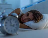 Una mujer en su cama mirando el despertador.