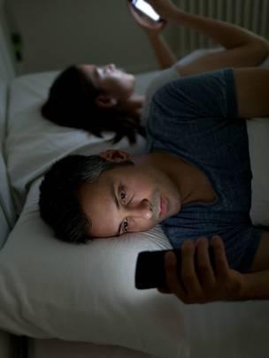 Un hombre usando el celular, mientras su pareja intenta dormir.