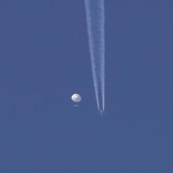 Un gran globo se desplaza por encima de la zona de Kingstown, Carolina del Norte, mientras por debajo se observa un avión y la estela que deja a su paso.