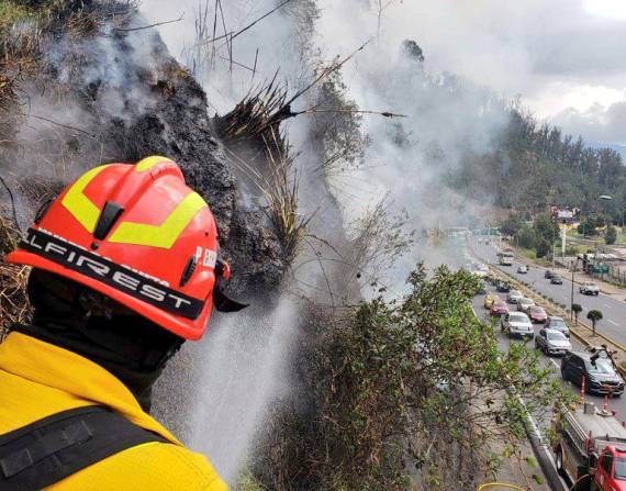 Momento en el que los bomberos apagan el fuego en el talud de la autopista General Rumiñahui.