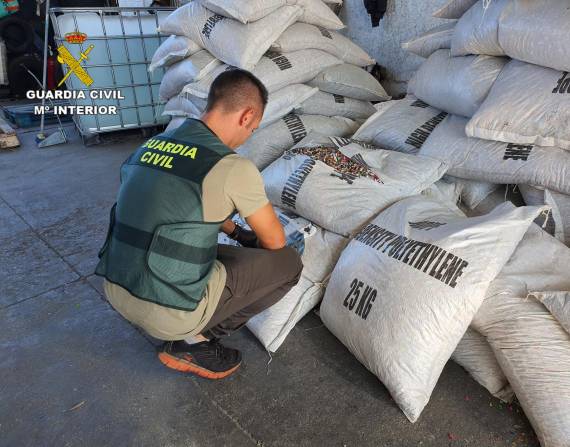 Un agente de la Guardia Civil revisa uno de los sacos de escamas multicolor de PET tereflalato de polietileno, incautados. EFE/ Guardia Civil