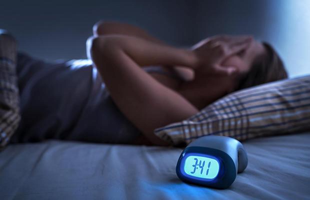 Una mujer en su cama junto a un despertador.