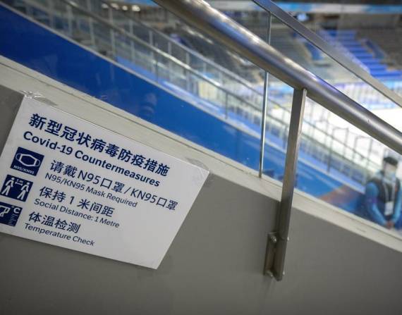 En esta imagen de archivo, un miembro del equipo, junto a un cartel con las normas de protección contra el COVID-19, durante la celebración del evento de prueba de hockey sobre hielo previo a los Juegos Olímpicos de Invierno de Beijing 2022, en el Estadio Nacional Indoor, en Beijing, el 10 de noviembre de 2021.