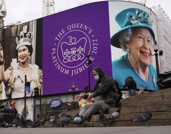 Un hombre alimenta a las palomas y a sus espaldas se ve una pantalla en Piccadilly Circus para celebrar el 70 aniversario del ascenso al trono de la reina Isabel de Gran Bretaña, en Londres, el domingo 6 de febrero de 2022.