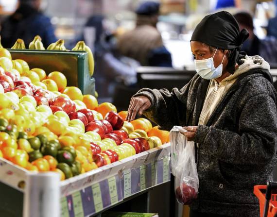 Una mujer con una mascarilla para el coronavirus selecciona frutas en el mercado de Reading Terminal en Filadelfia.