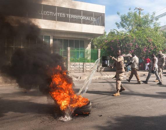 Un policía trata de apagar un neumático que un hombre prendió fuego enfrente del Ministerio de Interior de Haití .