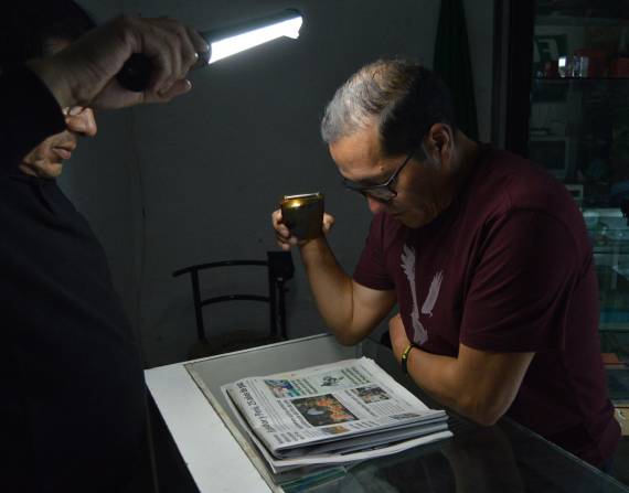 Imagen referencial de una persona alumbrando un periódico con la luz de su celular.