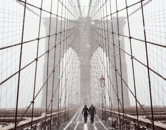 Fotografía de archivo en la que se registró a un par de transeúntes al cruzar el puente de Brooklyn, bajo una tormenta de viento y nieve, en Nueva York