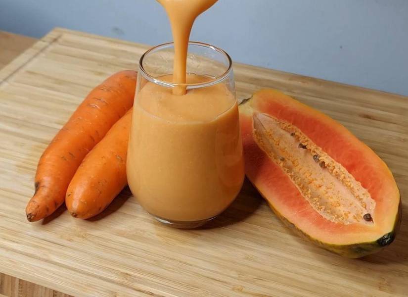 Imagen descriptiva de un vaso de jugo de zanahoria con papaya en tabla de madera