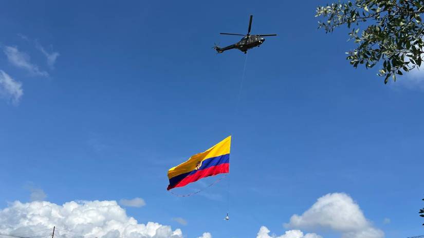 De un helicóptero militar cuelga una bandera de Ecuador.