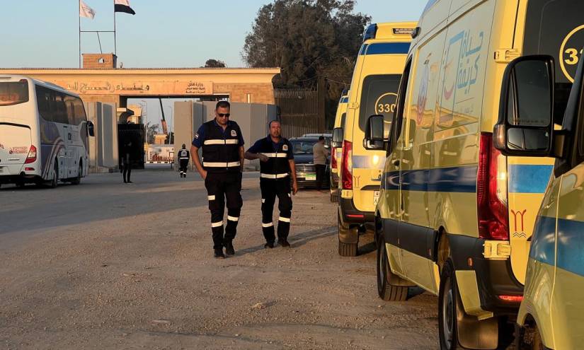 Los trabajadores de la Organización Egipcia de Ambulancias pasan junto a ambulancias estacionadas cerca del cruce fronterizo de Rafah entre la Franja de Gaza y Egipto, el corredor de evacuación.