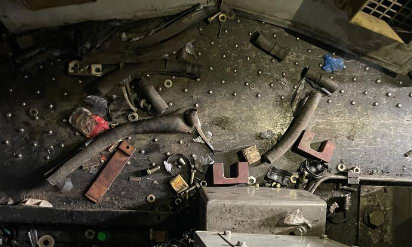 Junto al motor de un ferrocarril hay piezas botadas sobre piso. Todo destruido.