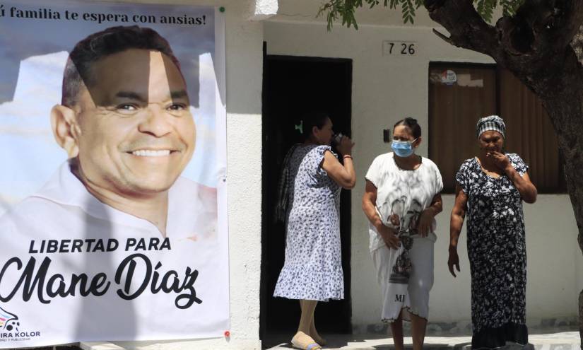 Varias personas salen de la casa familiar del futbolista colombiano Luis Díaz, de donde cuelga un gran cartel con la imagen de su padre, Luis Manuel Díaz.