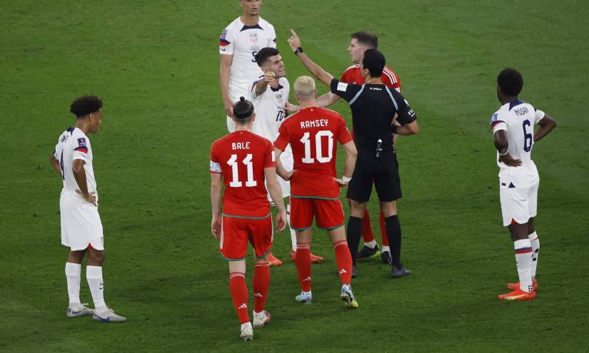 Los jugadores de Gales y Estados Unidos rodean al juez central mientras mantiene comunicación con la cabina del VAR.