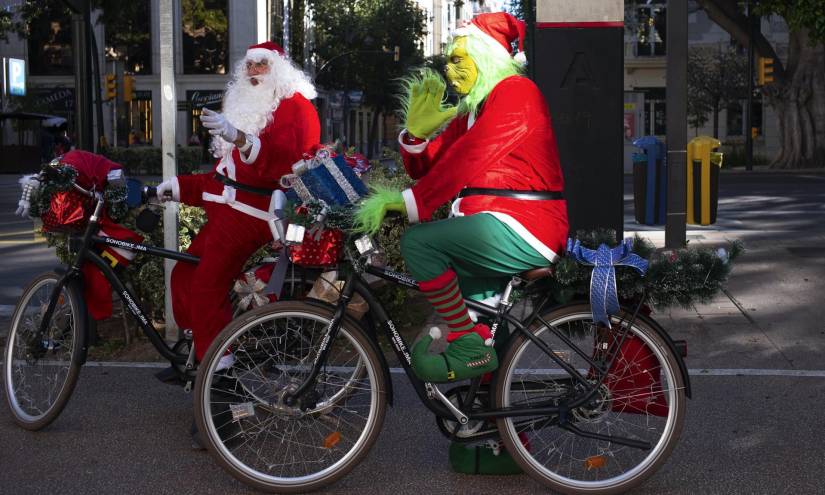Un hombre vestido de Papá Noel y otro del también popular personaje de navidad Grinch saludan a los viandantes en el centro de Málaga este domingo 24 de diciembre.
