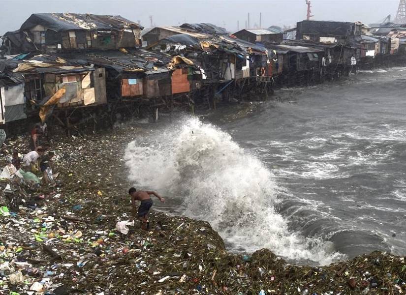 Un hombre se ve sorprendido por una ola mientras rescata materiales desperdigados por la orilla en Manila Bay, Filipinas.
