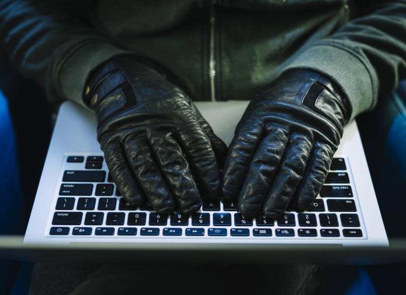 Persona con guantes escribiendo en su computadora.
